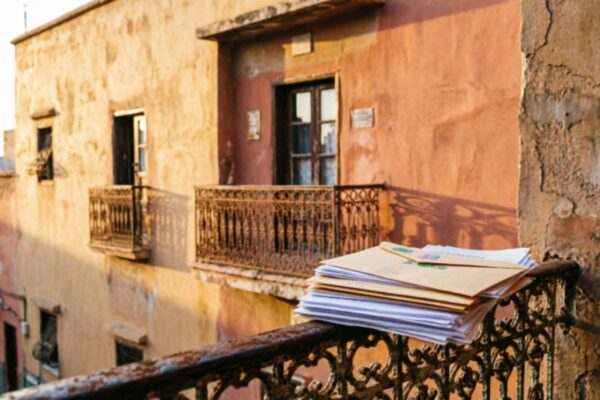 واجهة عمارة سكنية مغربية بألوان ترابية دافئة مع أوراق إدارية موضوعة على درابزين شرفة، ترمز لموضوع ضريبة السكن والإشعارات الضريبية